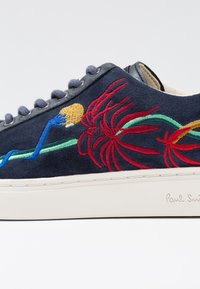 Navy suede sneaker with white sole, featuring colorful floral embroidery in red, green, and blue. Highlights include textured detailing and lace loops.