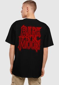 Sort oversized t-shirt med dristig rød, spids skrifttype med teksten "BARK AT THE MOON" på ryggen. 100% bomuldsstof med en glat overflade.
