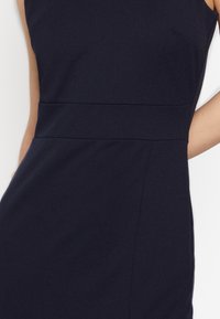 Vestido ajustado azul marino con una tela lisa y texturizada. Presenta un escote alto y una costura horizontal en la cintura, creando una silueta entallada.