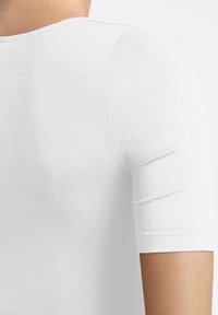 Vit kortärmad fitted skjorta, slät textur, rund halsringning, synliga sömdetaljer, och en närbild från baksidan.