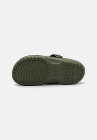 Semelle de chaussure en caoutchouc vert avec un motif de semelle texturé, présentant un logo en relief et une sangle noire attachée près du talon pour un maintien sécurisé.
