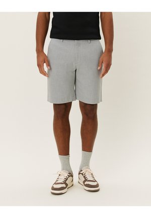 Pantaloni corti grigi chiari con una vestibilità sartoriale, frontale plissettato e tasche laterali, abbinati a scarpe da ginnastica marroni e crema e calzini grigi chiari.