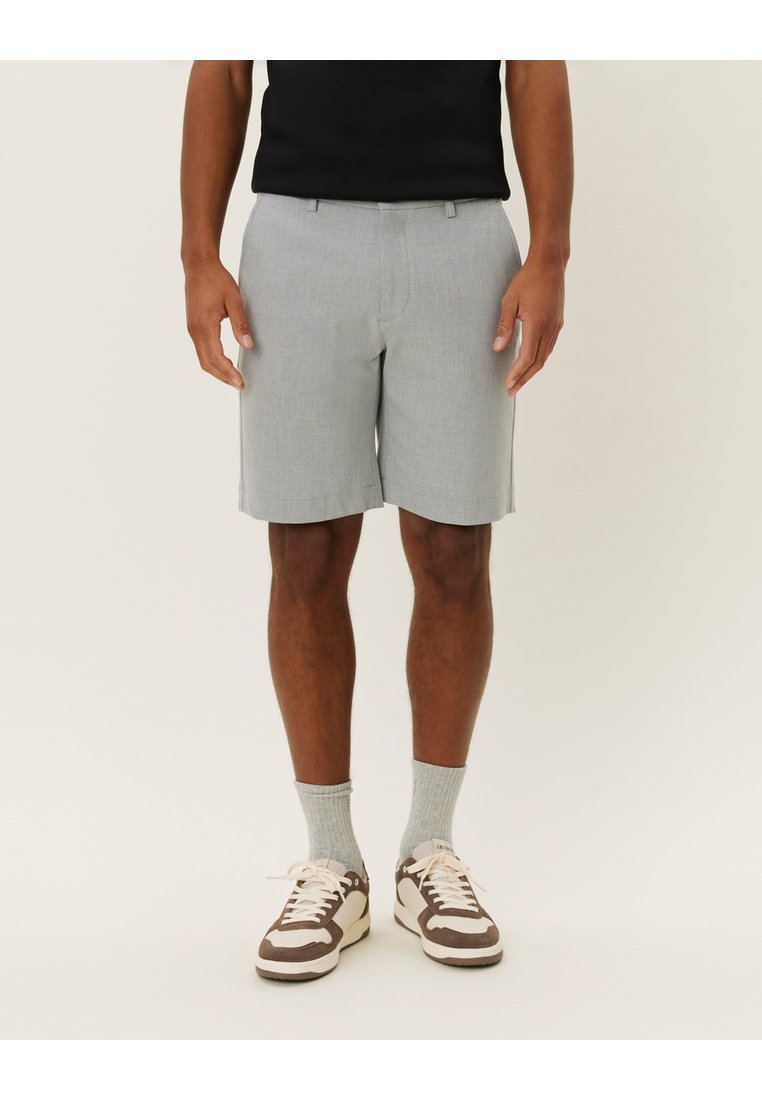Lys grå shorts med tilpasset passform, plisserte foran og sidelommer, kombinert med brune og kremfargede joggesko og lysegrå sokker.
