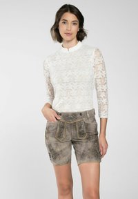 Haut en dentelle blanche à manches longues avec un col haut, associé à un short en suède gris orné de broderies florales et d'accents dorés sur les poches.