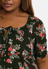 Svart blommig blus med rosa och röda blommor. Har en rund hals med en knytdetalj och elastiska ärmar för en avslappnad passform.