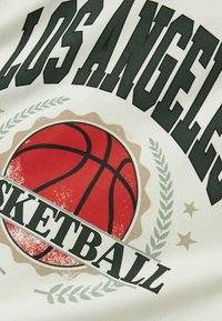 Tissu blanc avec un graphique de basketball rouge, texte noir avec "LOS ANGELES" et "BASKETBALL", entouré de branches de laurier vertes et d'étoiles.