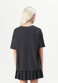 Dark gray t-shirt with short sleeves, round neckline, soft texture, and relaxed fit, paired with a pleated black skirt.