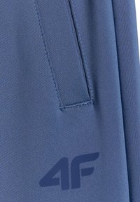 Gros plan sur un tissu bleu montrant un détail de patch rectangulaire cousu et un logo "4F" bleu foncé imprimé près du coin inférieur droit.