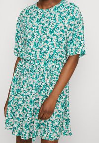 Vestido de manga corta en tejido ligero, con un patrón floral en tonos verdes, rosas y blancos. Cintura elástica y falda acampanada.