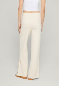 Kremowe spodnie w szerokim kroju z elastycznym paskiem, z bocznymi rozcięciami na dole i gładką, miękką teksturą.