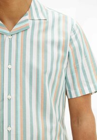 Koszula na krótki rękaw z guzikami w kolorach jasnoniebieskim, białym i brzoskwiniowym, z pionowymi paskami i fakturowaną tkaniną oraz płaskim kołnierzykiem.