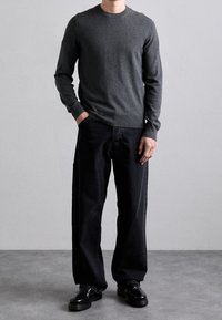 Grå stickad tröja med rund halsringning i kombination med löst sittande svarta jeans. Utseendet fulländas med glansiga svarta skor.