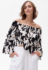 Bluzka na ramiączkach z czarno-białym wzorem kwiatowym. Miękka tkanina, rozszerzane rękawy, szczegół w formie węzła z przodu. Połączona z białymi spodniami.