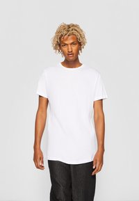 Weißes Baumwoll-T-Shirt mit Rundhalsausschnitt und kurzen Ärmeln, das einen lässigen Schnitt und eine glatte Textur aufweist, getragen mit dunklen Hosen.
