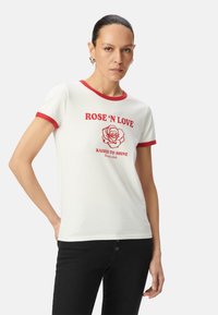 Camiseta blanca con detalles en rojo, que presenta "ROSE 'N LOVE" y un gráfico de rosa impreso en rojo. Diseño ajustado con mangas cortas.