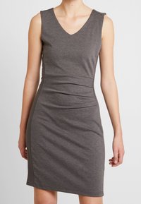 Robe grise ajustée en tissu doux et extensible. Présente un décolleté en V profond, un design sans manches et un détail froncé sur le côté pour mettre en forme.