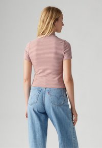 Randig kortärmad topp i korall och vitt; figursydd design. Matchas med ljusblå högmidjade jeans med klassiska bakfickor.