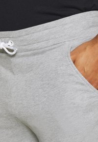 Pantalones de chándal gris claro con una textura suave, cintura elástica y cordón ajustable. Presenta bolsillos laterales y un corte relajado.