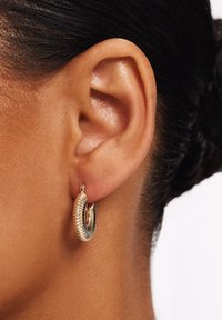 Oorringen in goudkleur met een geribbelde textuur en een spiraalvormig ontwerp. De oorringen zijn bevestigd aan een klein hefboomsluiting.