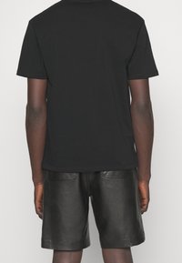 Svart t-shirt med kort ärm kombinerad med svarta lädershorts med en slät yta och två bakfickor, sedd bakifrån.