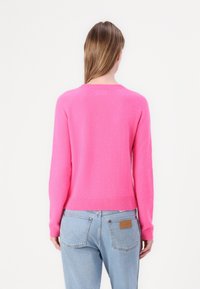 Lys rosa genser med rund hals og ribbestrikket kant og mansjetter, laget av mykt materiale. Brukt over lys blå jeans med lommer og merkelapp.
