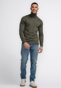 Olijfgroene coltrui, slim fit, geribbelde manchetten en onderrand, gecombineerd met lichtblauwe spijkerbroek en beige sneakers met witte veters en tan zolen.