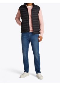 Czarna pikowana kamizelka puchowa, różowa bluza z długim rękawem, niebieskie dżinsy i białe trampki. Gładka faktura i dopasowany krój.