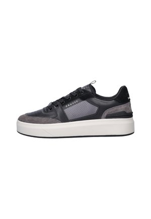 Zwart-grijze lage sneaker met een dikke witte zool, veters aan de voorkant, een gestructureerd zijpaneel en een gebrandmerkt "Cruyff" detail.