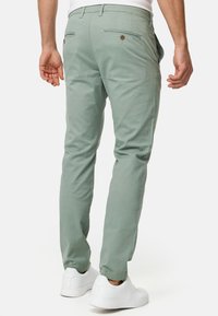 Chinos de algodón verde claro con un ajuste slim, bolsillos traseros con cierre de botón y combinados con zapatillas blancas.