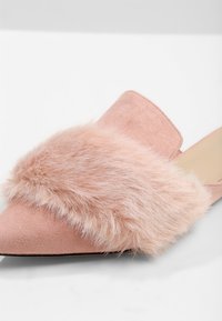 Mule pointue en daim rose avec une large bride en fausse fourrure rose douce sur le dessus, dos ouvert et petit talon.