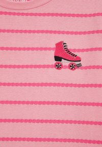 Růžové pruhované tričko z látky s vodorovnými vzory; na levé straně má vyšitý obrázek kolečkového brusle v růžové a černé barvě.