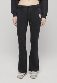 Czarne rozkloszowane spodnie dresowe o miękkiej fakturze, z elastycznym paskiem i sznurkiem do regulacji. Na biodrze znajduje się małe białe logo.