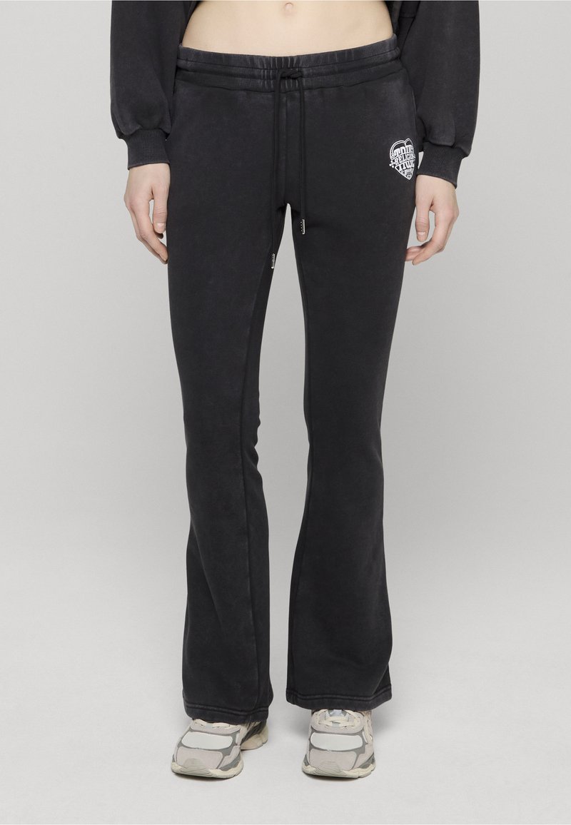 Czarne rozkloszowane spodnie dresowe o miękkiej fakturze, z elastycznym paskiem i sznurkiem do regulacji. Na biodrze znajduje się małe białe logo.