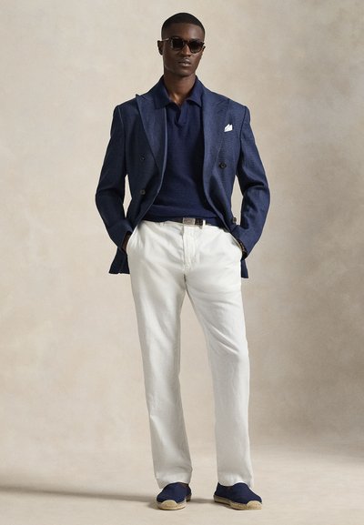 Ναυτικό σακάκι με υφή υφάσματος, σκούρο πόλο, λευκό παντελόνι και μπλε εσπαντρίγιες με μπεζ σόλες. Τα γυαλιά ηλίου συμπληρώνουν την εμφάνιση.