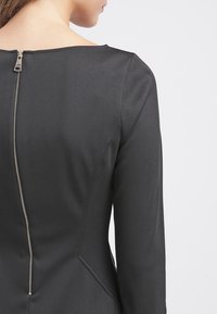 Abito nero con un tessuto liscio, design aderente e maniche lunghe. Presenta una cerniera metallica visibile sul retro e una semplice forma del collo.