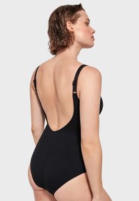 Maillot de bain une pièce noir avec bretelles réglables, design à dos nu et texture côtelée. Pas de motifs visibles ni de détails en métal.