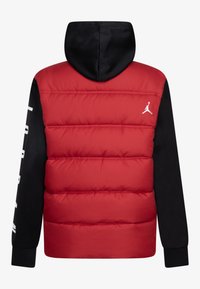 Veste doudoune rouge avec une capuche et des manches noires. Présente des sections matelassées horizontales et un logo blanc sur la poitrine. Accents de couleur unie.
