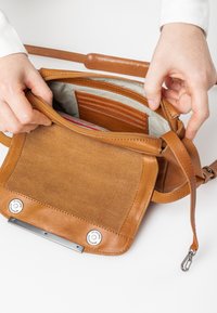Tasche aus braunem Leder mit verstellbarem Schulterriemen, ausgestattet mit einem gefütterten Innenraum, vertikalen Kartenfächern und einem magnetischen Druckverschluss.