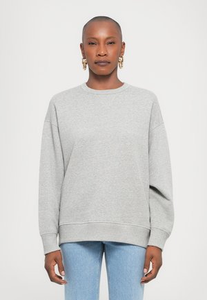 Lys grå genser med rund hals, senket skuldre og ribbede mansjetter. Parret med lyseblå denimjeans.