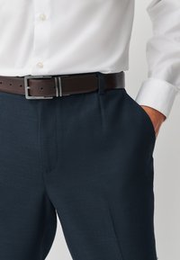 Dark blue textured trousers with side pockets, worn with a white button-up shirt and a brown leather belt featuring a silver buckle.