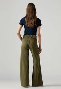 Jeans de pierna ancha color verde oliva con cintura alta, logo de parche en la parte trasera y costuras dobles. Combinados con una camiseta ajustada de color azul marino.