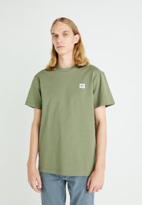 T-shirt in cotone verde oliva con colletto tondo e maniche corte, con un piccolo etichetta bianca sul lato sinistro del petto. Vestibilità regolare.