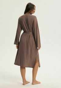 Brązowy, długi szlafrok z długim rękawem, wykonany z miękkiego materiału, z paskiem w talii i bocznymi rozcięciami, sięga poniżej kolana, o gładkiej fakturze.