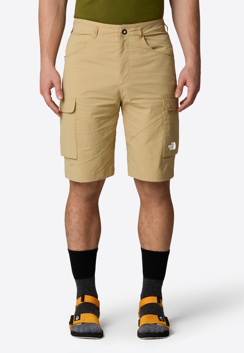 Pantaloni cargo beige in un materiale leggero, dotati di tasche frontali e laterali, dettagli cuciti e un logo sulla gamba destra.