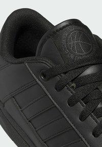 Černé kožené tenisky mají strukturovaný svršek, silné tkaničky a polstrovaný límec. Mezi výrazné detaily patří vyvýšené logo a horizontální pruhy.