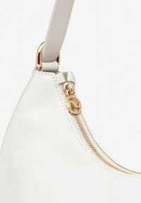 Sac à main en cuir blanc avec un design incurvé, quincaillerie dorée et fermeture éclair avec un tirette décorative.