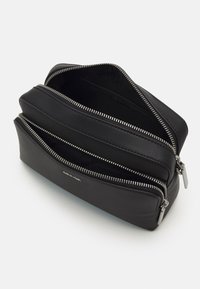 Pochette in pelle nera con due scomparti con cerniera. Presenta ferrature argentate e un logo in rilievo. Texture liscia e forma rettangolare.