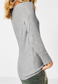 Grauer Pullover mit langen Ärmeln und geripptem Halsausschnitt und Bündchen. Weicher, strukturierter Stoff mit lockerer Passform. Seitliche Schlitze für zusätzlichen Stil.