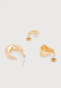 Tres pendientes de aro en tono dorado sobre fondo blanco; uno liso, uno ondulado y uno engastado con pequeños cristales claros.