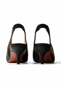 Pár fekete slingback kismacskás cipő hegyes orral és alacsony, keskenyedő sarkakkal, hátulról fehér háttér előtt.